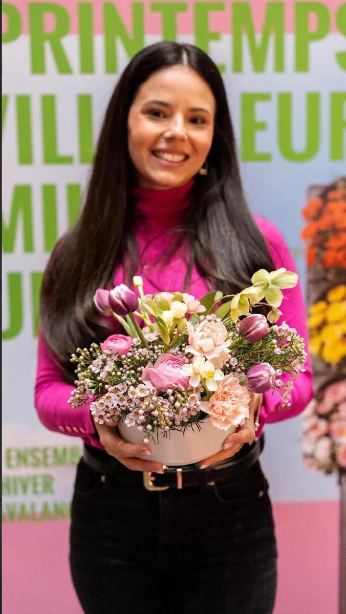 Amanda Berton souriante à un marché aux fleurs, un arrangement floral dans les mains
