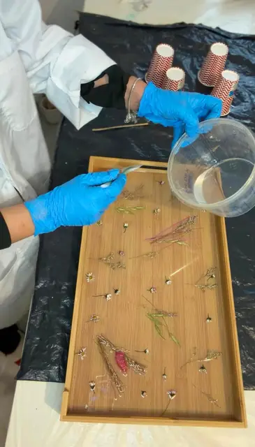 Mains gantées versant de la résine sur un plateau garni de fleurs