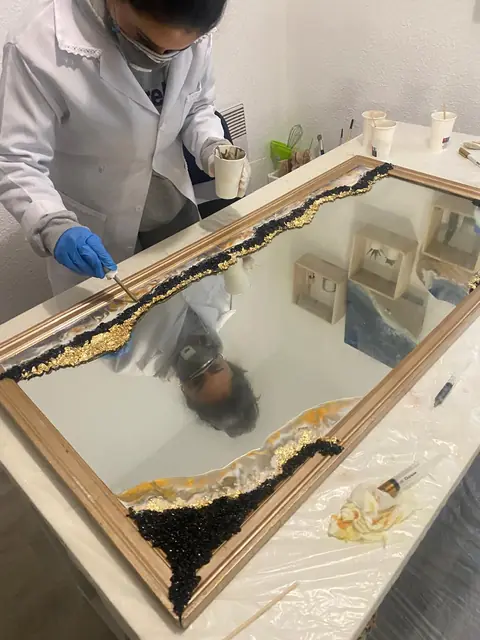 Amanda Berton appliquant de la feuille d'or sur un cadre miroir, en blouse et masque