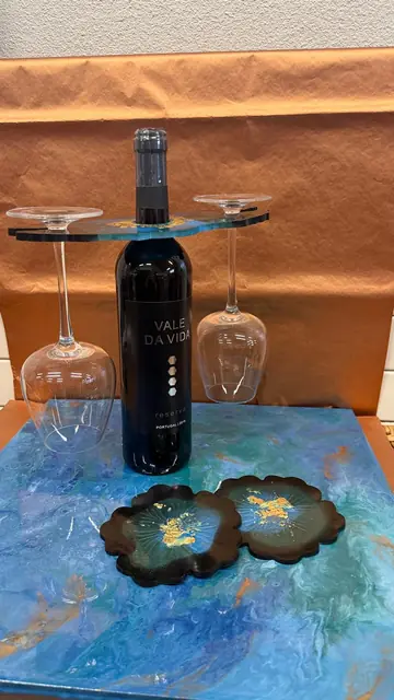 Porte bouteille en résine bleu profond tenant une bouteille et deux verres, avec deux sous verres en forme de fleur, posé sur une toile peinte